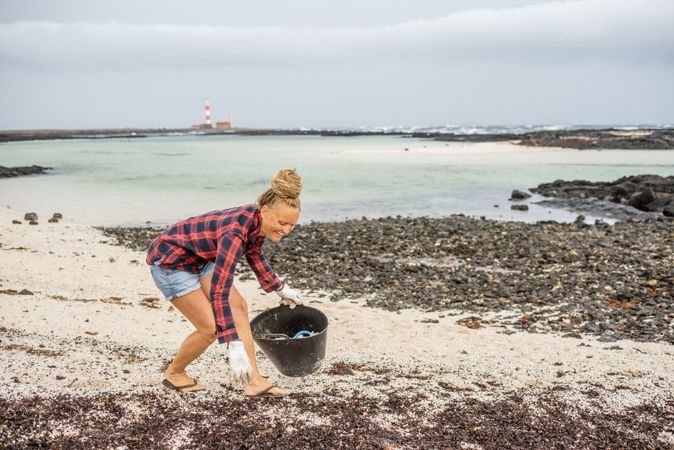 Content modern woman picking litter from sandy seashore