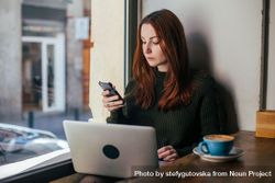 Woman checking phone in cafe with laptop 49Pwn5