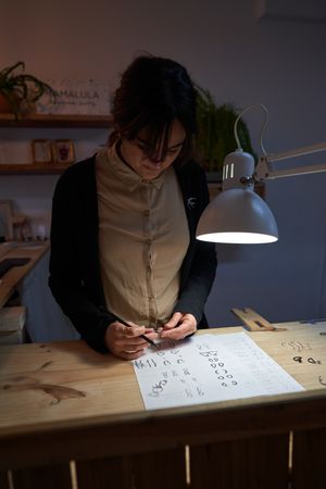 Focused female jeweler with ring and sketches at table