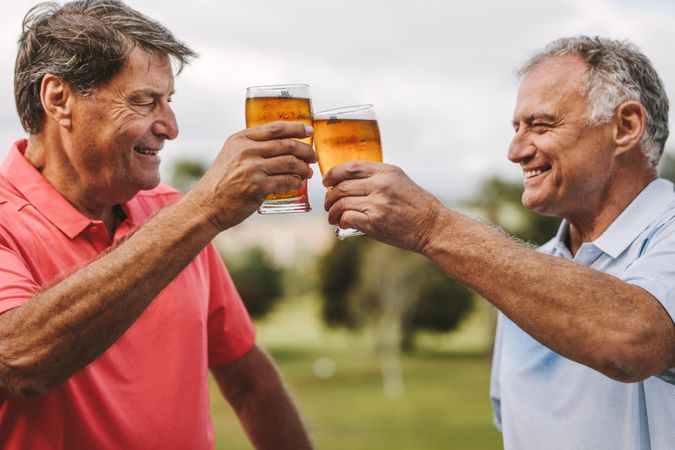 Two mature men toasting beer glasses outdoors