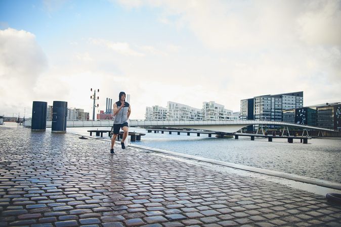 Athletic male jogging near river outside on chilly day