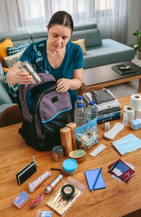 Woman putting cans of food to prepare emergency backpack