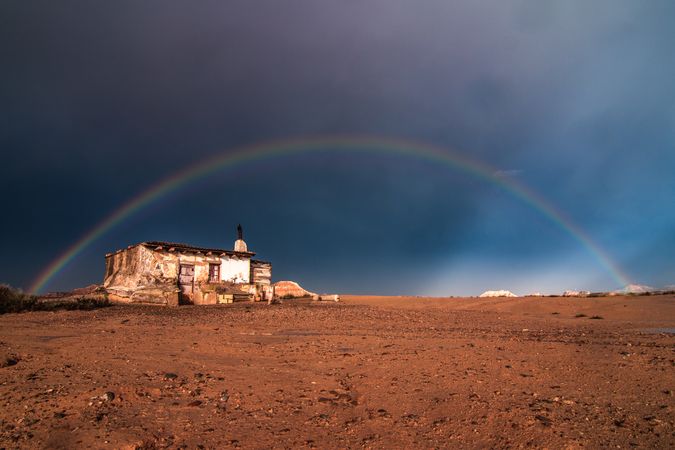 Lonely house in desert and rainbow in sky