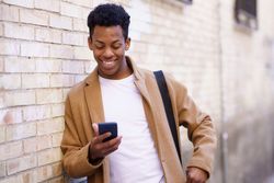 Happy Cuban male leaning against wall looking down at his phone