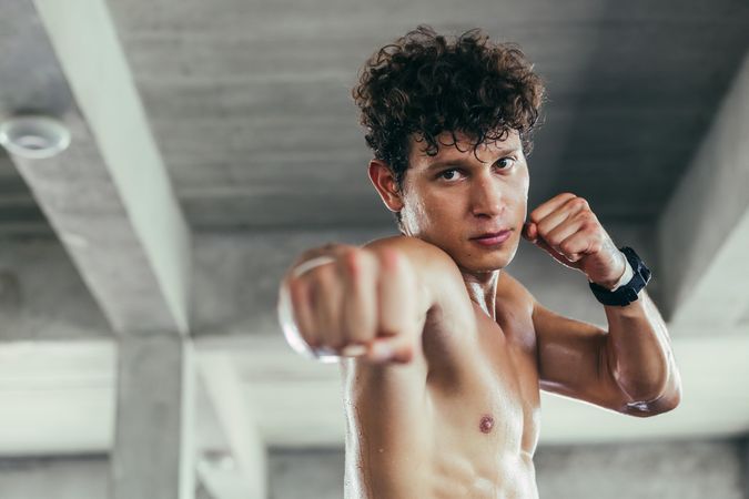 Brown haired male looking in camera in gym and punching