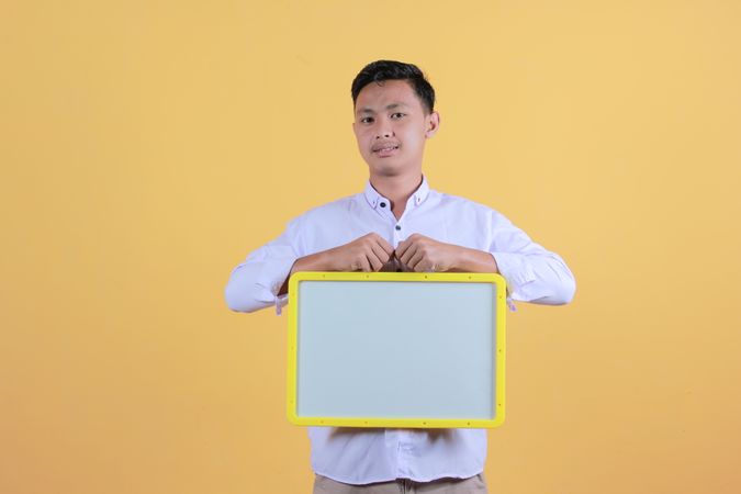 Portrait a young man in yellow backdrop holding a blank note board