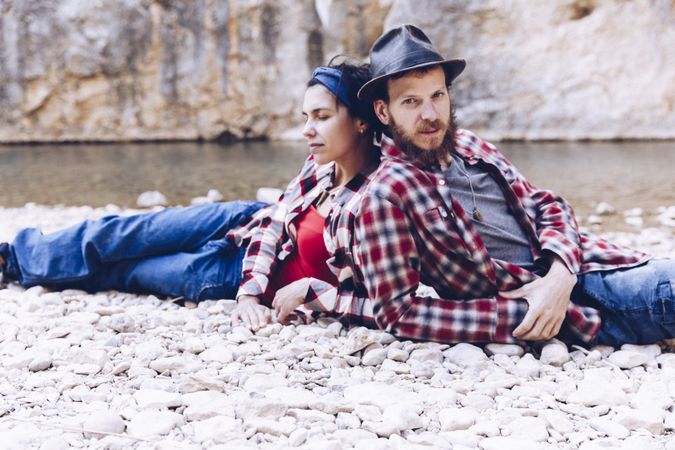 Positive woman and man resting on stone shore near river