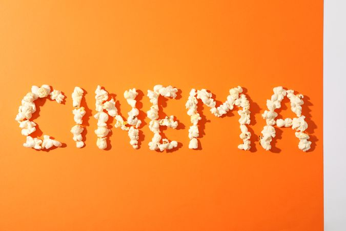 Word cinema laid out from popcorn on orange background, copy space