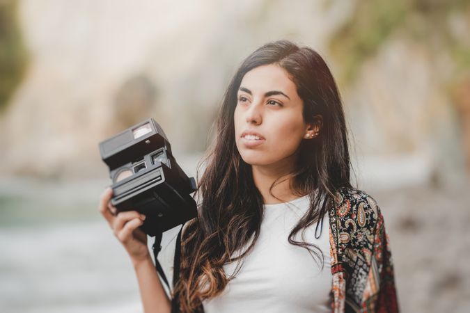 Woman with camera on shore near stones and water