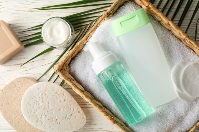Body care accessories and palm leaf on wooden background, top view