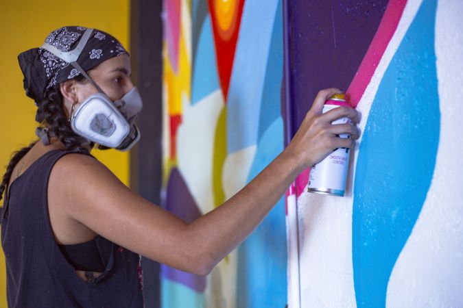 Side view of woman with bandana and gas mask creating a mural graffiti on wall