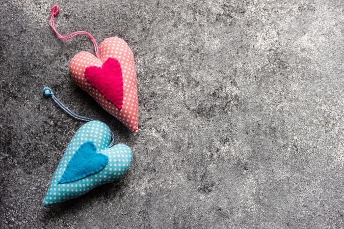 Two blue and pink felt heart ornaments on grey counter with copy space