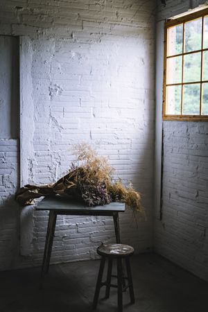 Bunch of plant in paper on table near stool in grey room