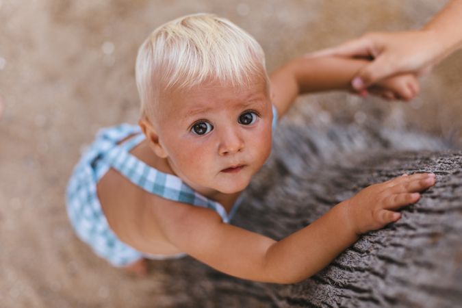Top view of a blonde baby on the beach.to a tree