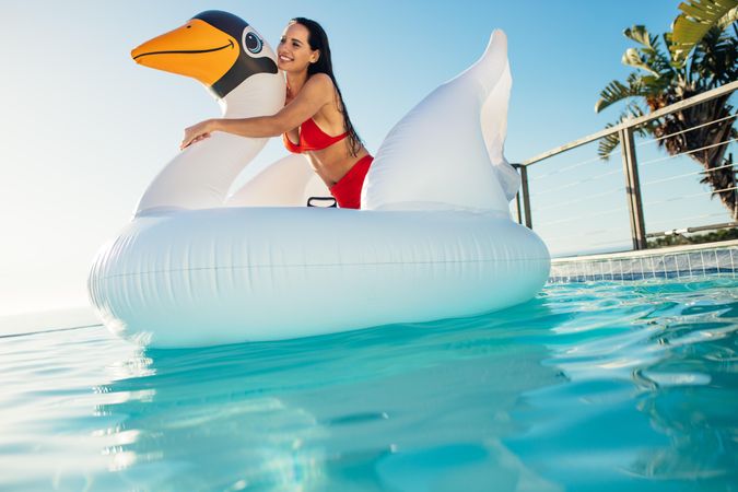 Beautiful woman enjoying her vacation in a swimming pool with inflatable swan