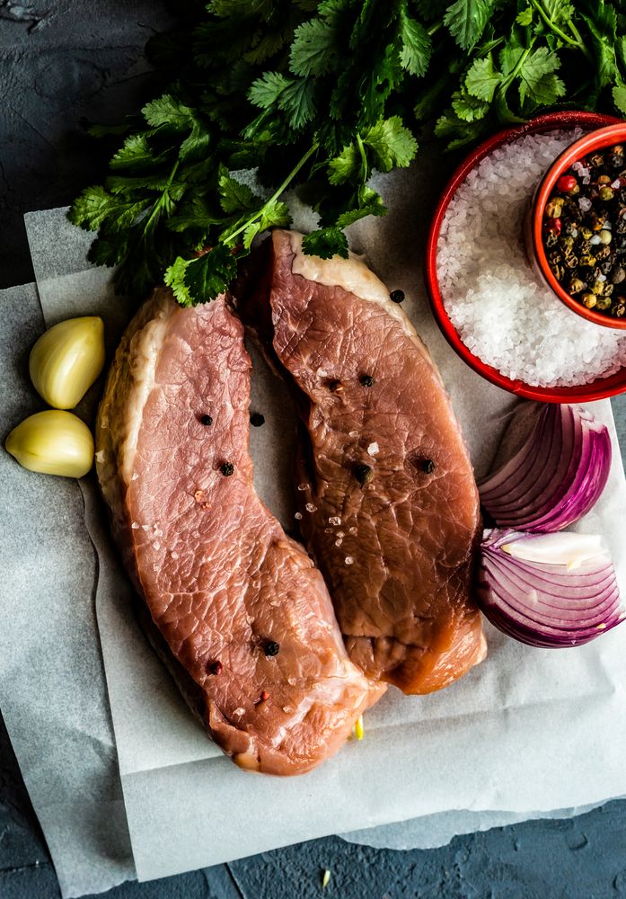 Top view of two raw pork chops with onion, garlic and herbs