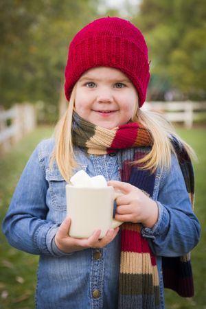 Cute Young Girl Holding Cocoa Mug with Marsh Mallows Outside