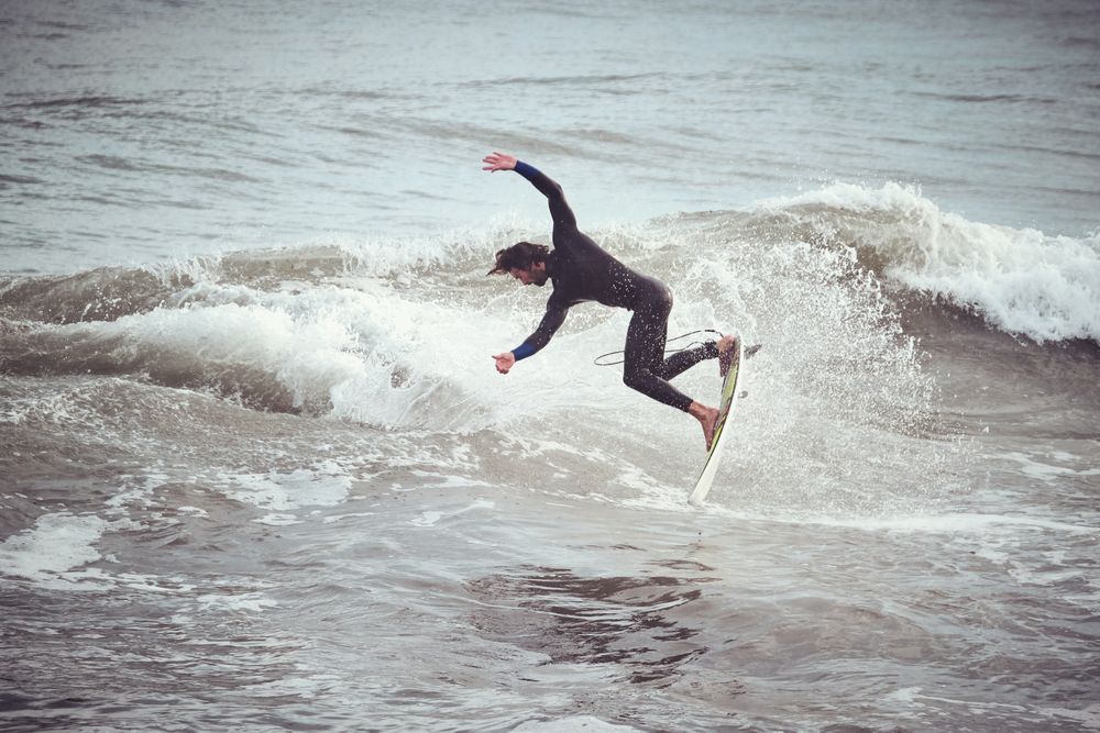 Surfer male jumping on wave standing on surfboard in ocean