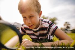 Boy looking through magnifying glass in the grass on a sunny day bYX994