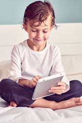 Smiling boy with wet hair browsing tablet on bed