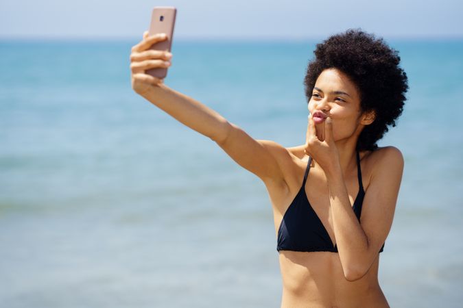 Woman in bikini taking funny selfie on phone on coast