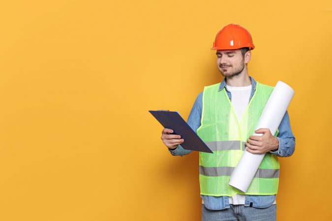 Engineer in helmet with paper and folder in hands on yellow background, space for text