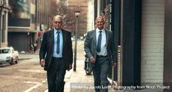 Two mature business people walking down sidewalk 49oWL0