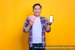 Smiling Asian man holding cash and showing blank phone screen in studio shoot bGwy2b