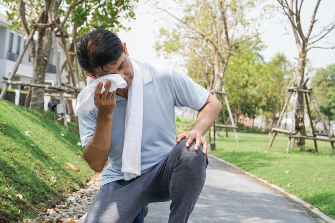 Male crouched on walkway wiping sweat during workout