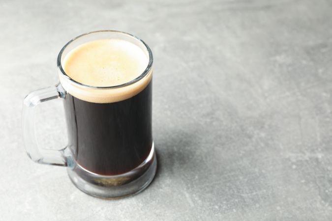 Glass of dark beer on grey background, space for text