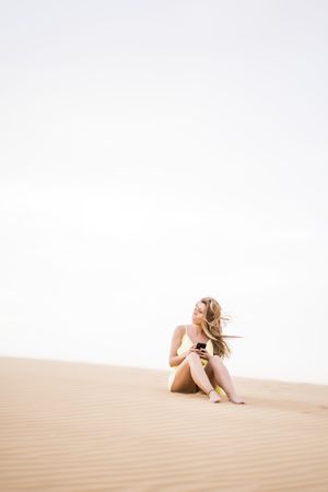 Thoughtful woman using smartphone in desert