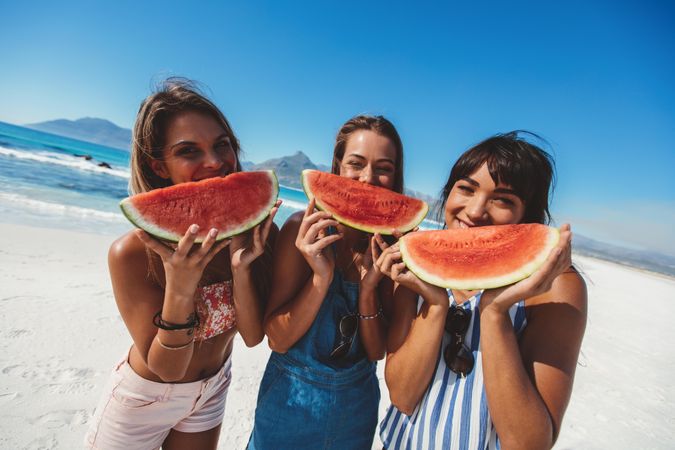 Female friends eating watermelon at the shore on summer day