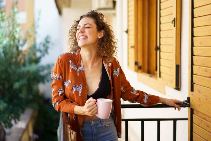 Laughing woman enjoying coffee in morning from balcony