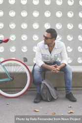 Relaxed male sitting with bike parked in front of patterned cement wall, vertical 0glZl5