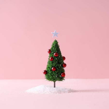 Christmas tree with red decorations with snow on pastel pink background