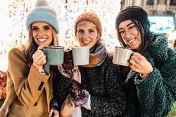 Three happy friends holding mugs and looking at the camera at a Christmas market.
