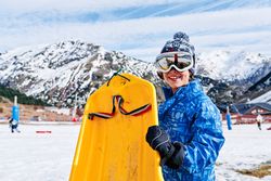 Friendly boy with sledge near snowy mountains