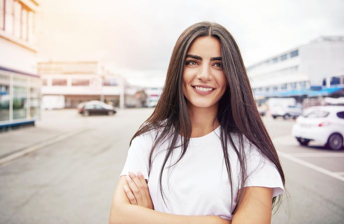 Relaxed smiling woman with long brown hair smiling standing in street with parked cards