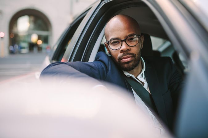 Handsome young Black man in suit leaning out of car window looking at camera