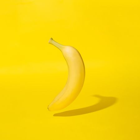 Single banana on yellow background with shadow