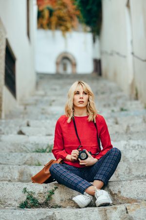 Blonde woman with red shirt sitting on steps outdoors with camera