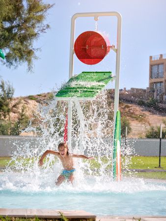 Shirtless boy jumping in pool during water fall from bucket abov