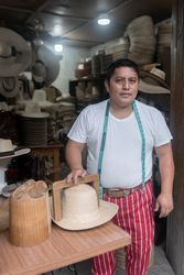 Portrait of an adult Hispanic tailor posing with a hat in his workshop