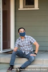 Man wearing PPE mask in casual clothing sitting on porch smiling and looking away 0KMw74