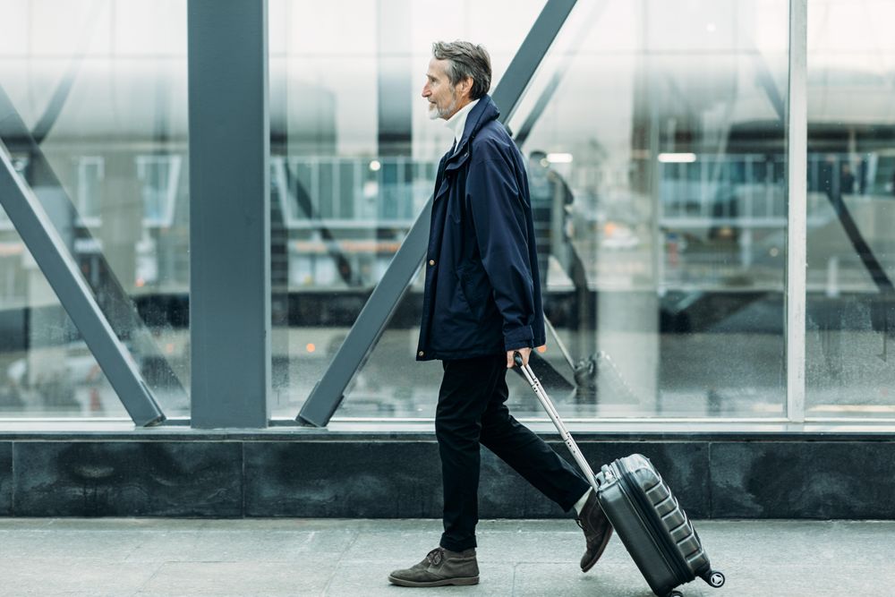 Older man crossing walkway in airport with carry on baggage