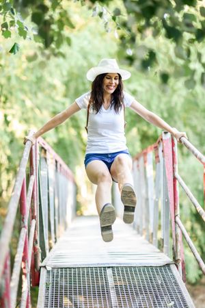 Smiling brunette female swinging herself on wooden bridge in forest