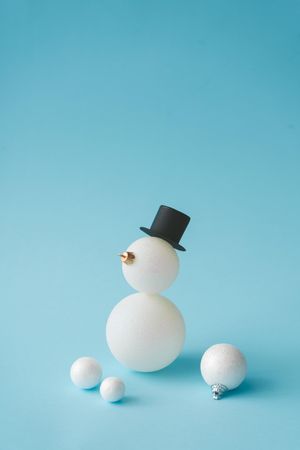 Snowman in top hat made of Christmas bauble decoration on pastel blue background