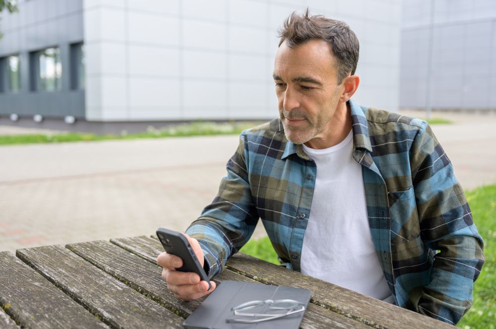 Concentrated man with smartphone and laptop in park