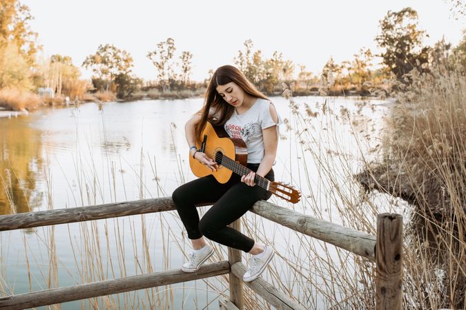 Young woman playing guitar near water