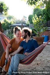 Woman looking lovingly at her partner sitting together outside in hammock 4MGml0